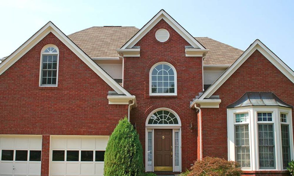 Red brick suburban house with large bay window and an elegant arched entryway on a sunny day.