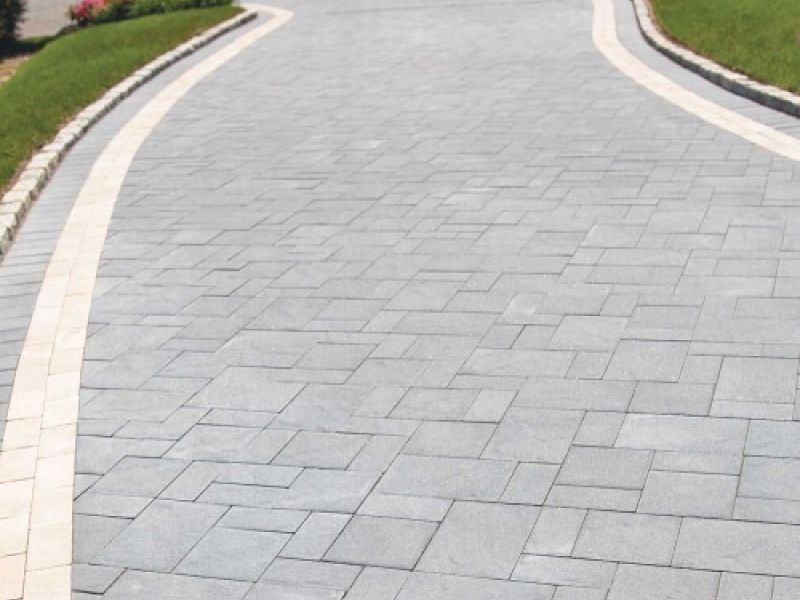 Elegant stone driveway with intricate patterns and lush green lawn borders under a clear sky.