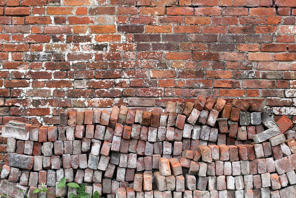 Old brick wall with moss and uneven bricks, showcasing rustic texture and vintage architecture.