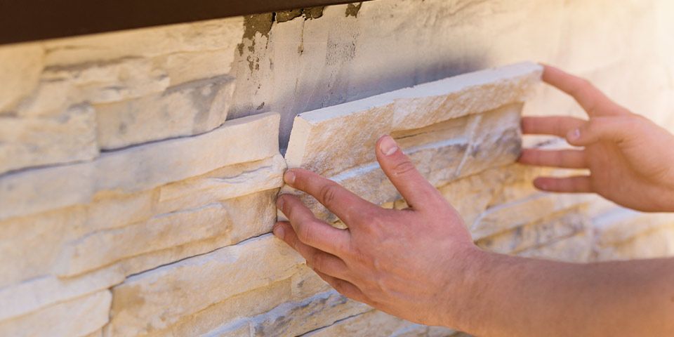 Hands placing stone veneer on exterior wall for home improvement.