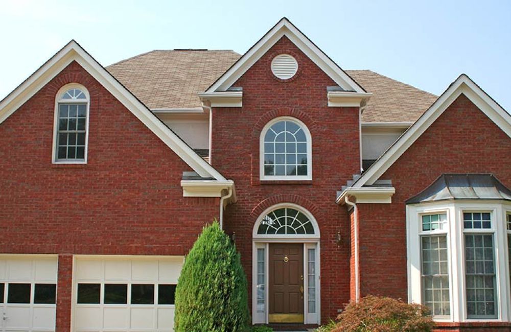 Red brick suburban house with large bay window and an elegant arched entryway on a sunny day.