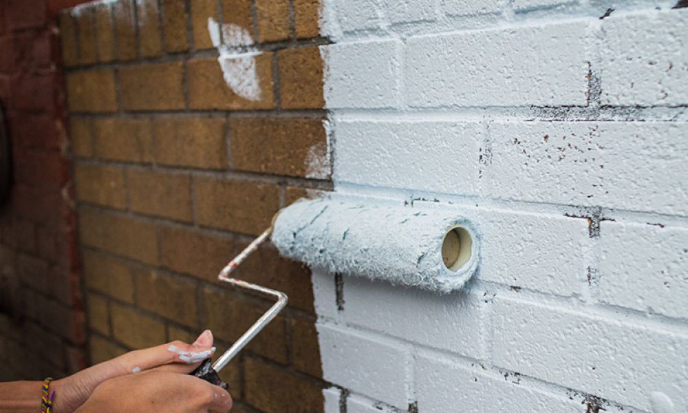 man painting a brick wall white