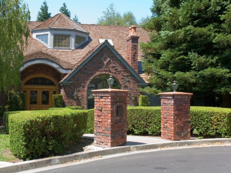Charming brick house with tall trees and manicured bushes, showcasing a welcoming suburban curb appeal.