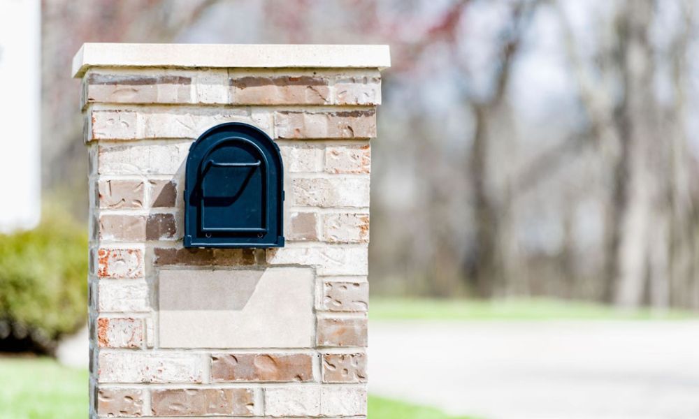 Black mailbox on a brick pillar in a suburban neighborhood.