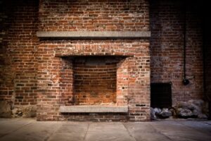 Historic exposed brick fireplace in an industrial-style setting, featuring vintage red brickwork and stone floor.