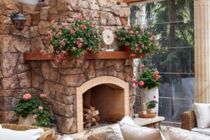 Cozy stone fireplace adorned with pink flowers and elegant decor in a sunlit room.