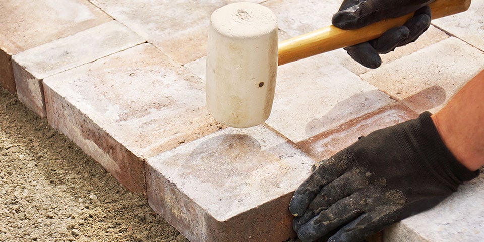 man using a mallet to set brick pavers