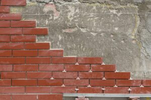 Red brick wall under construction with uneven cement background.
