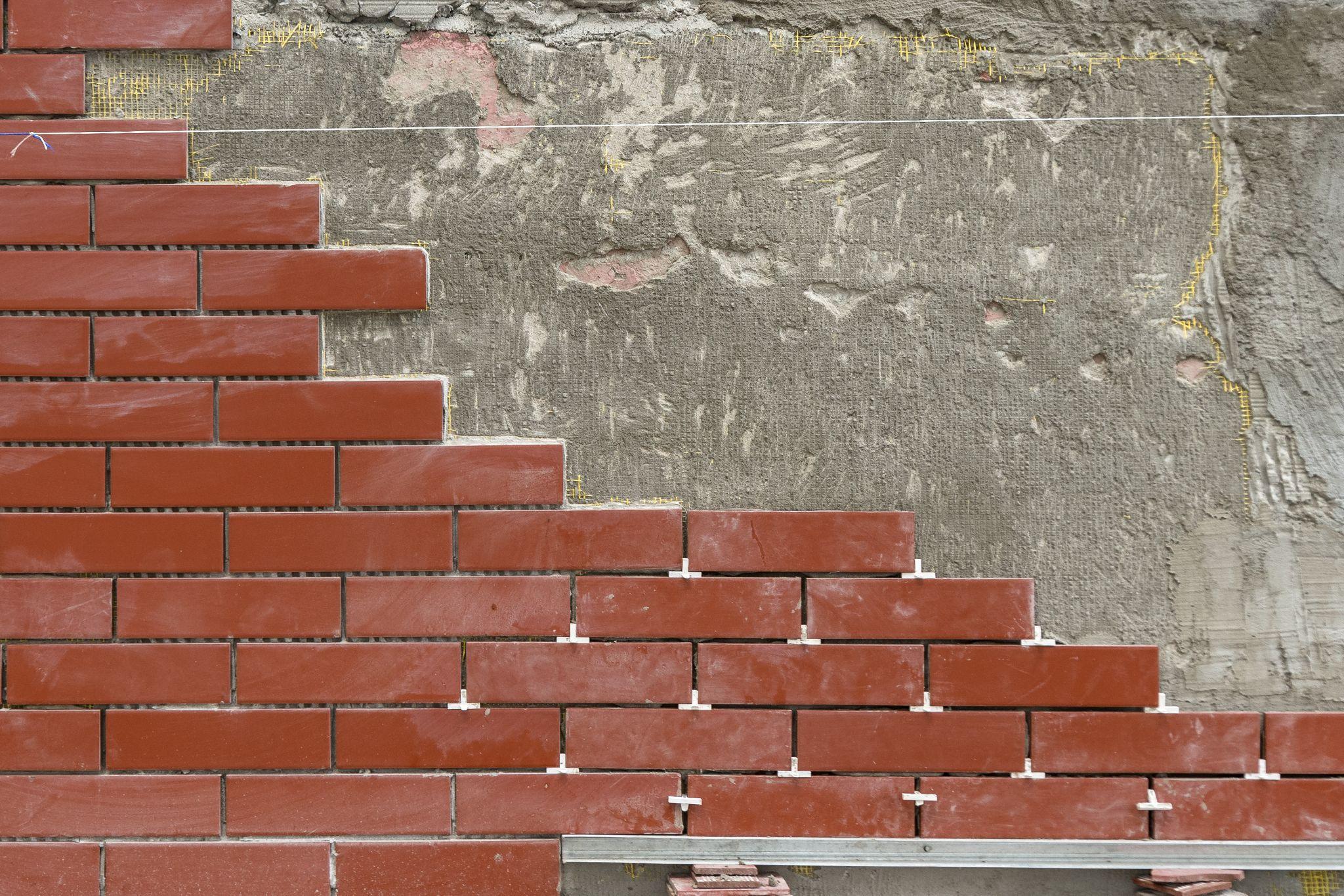 Red brick wall under construction with uneven cement background.