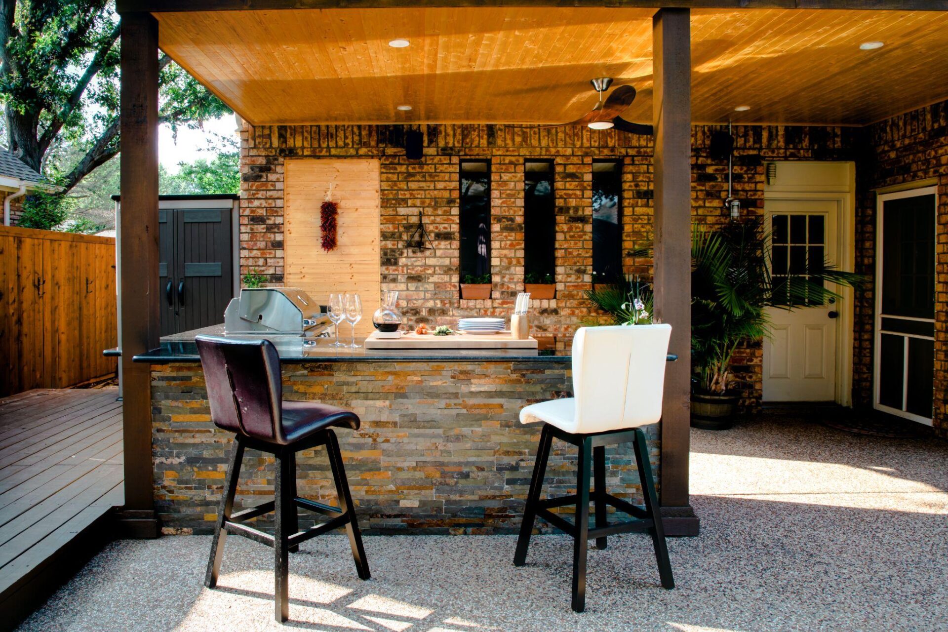 Outdoor kitchen with stone bar, two chairs, grill, and wooden ceiling, enhancing patio for entertaining and dining.