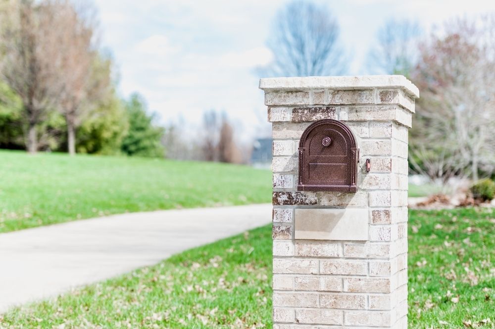 Brick mailbox on a sunny day with green grass and a winding path in the background, showcasing a serene suburban setting.