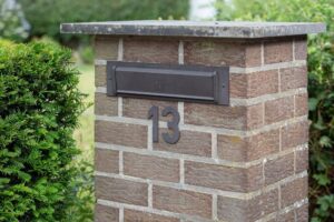 Brick mailbox pillar with house number 13, surrounded by green bushes. Ideal for suburban home imagery.