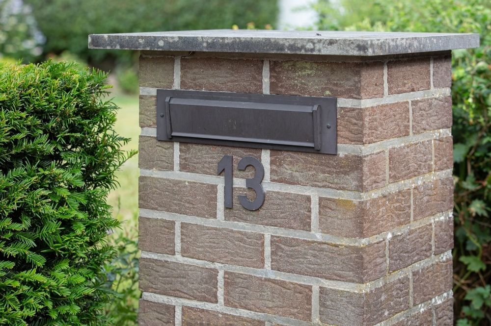 Brick mailbox pillar with house number 13, surrounded by green bushes. Ideal for suburban home imagery.