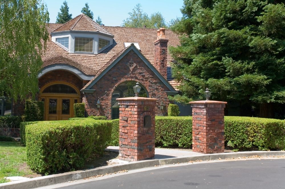 Charming brick house with tall trees and manicured bushes, showcasing a welcoming suburban curb appeal.